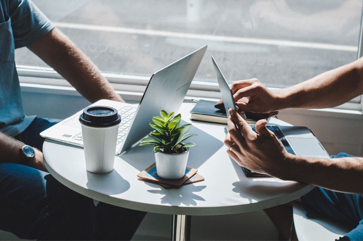 Two agents working on laptops and a tablet at a small office table
